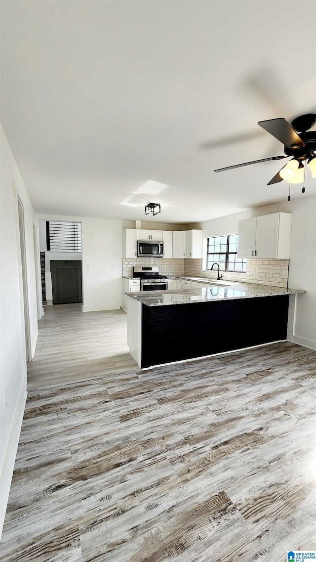 kitchen featuring light wood-type flooring, white cabinetry, decorative backsplash, and appliances with stainless steel finishes