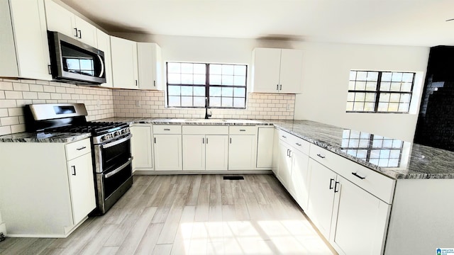 kitchen featuring a peninsula, appliances with stainless steel finishes, plenty of natural light, and dark stone countertops