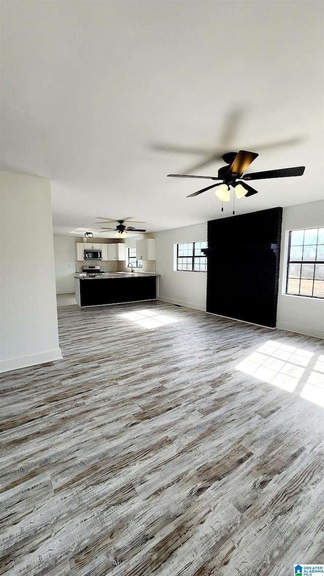 unfurnished living room with a sink, a ceiling fan, and light wood-style floors