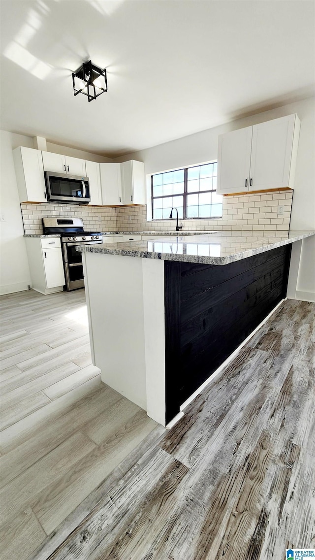 kitchen featuring tasteful backsplash, appliances with stainless steel finishes, white cabinetry, and light wood-style floors