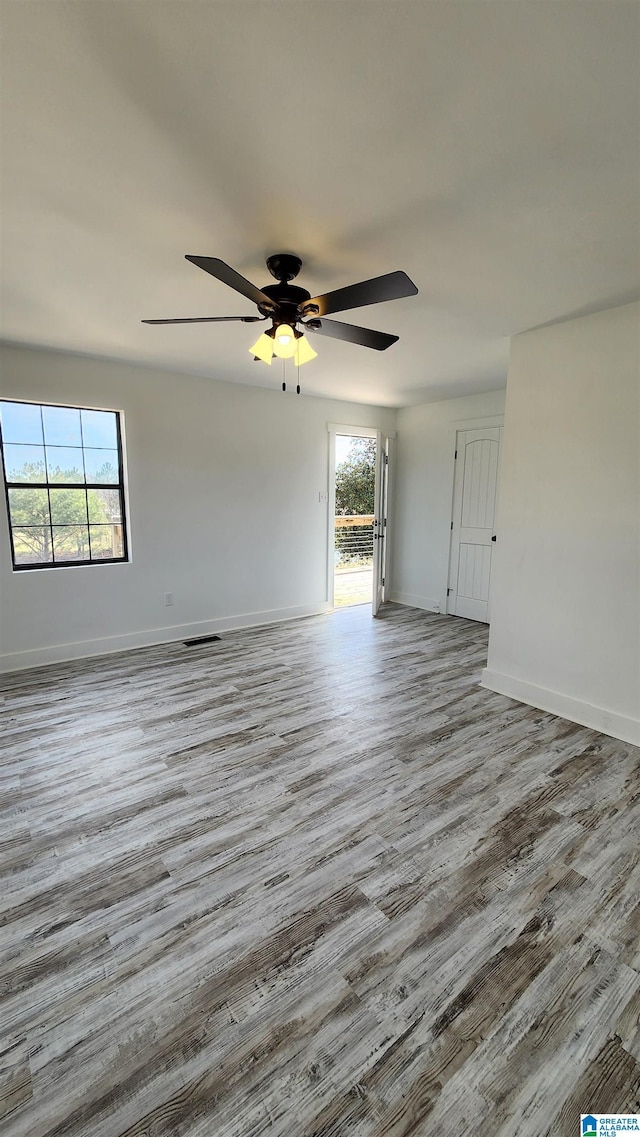 empty room featuring wood finished floors, ceiling fan, baseboards, and plenty of natural light