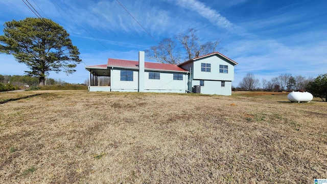 back of house featuring a sunroom, metal roof, a lawn, and a chimney