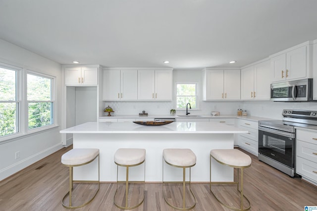 kitchen featuring a kitchen island, white cabinets, a kitchen bar, appliances with stainless steel finishes, and a sink