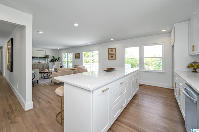kitchen with a center island, wood finished floors, stainless steel dishwasher, and white cabinets