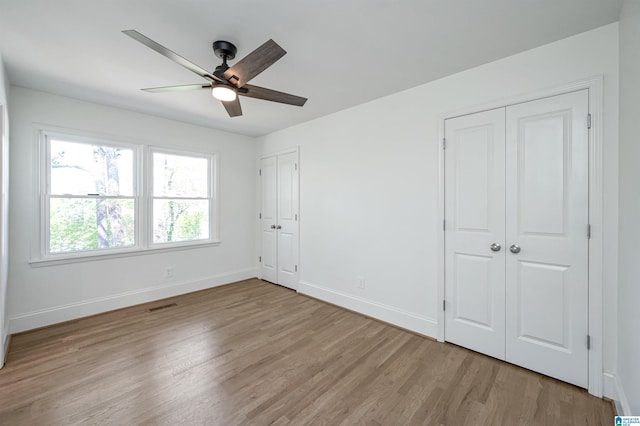unfurnished bedroom with light wood-style floors, baseboards, visible vents, and multiple closets