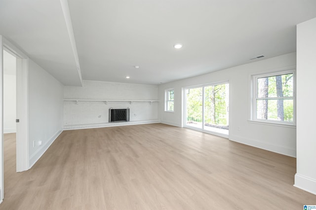 unfurnished living room featuring light wood-style floors, visible vents, baseboards, and a brick fireplace