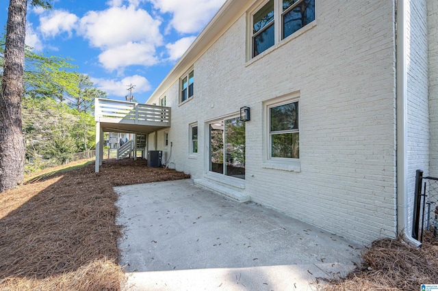 rear view of property featuring a patio, stairs, brick siding, central AC unit, and a wooden deck