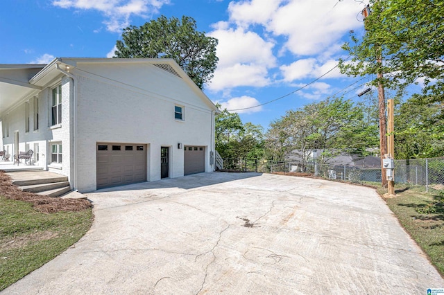 view of home's exterior featuring brick siding, driveway, fence, and an attached garage