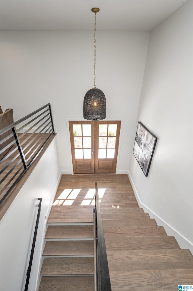 staircase with french doors, baseboards, a high ceiling, and wood finished floors