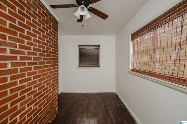 interior space with baseboards, brick wall, a ceiling fan, crown molding, and wood-type flooring