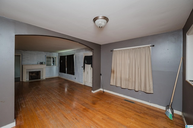 unfurnished living room featuring a fireplace with flush hearth, arched walkways, visible vents, baseboards, and hardwood / wood-style flooring