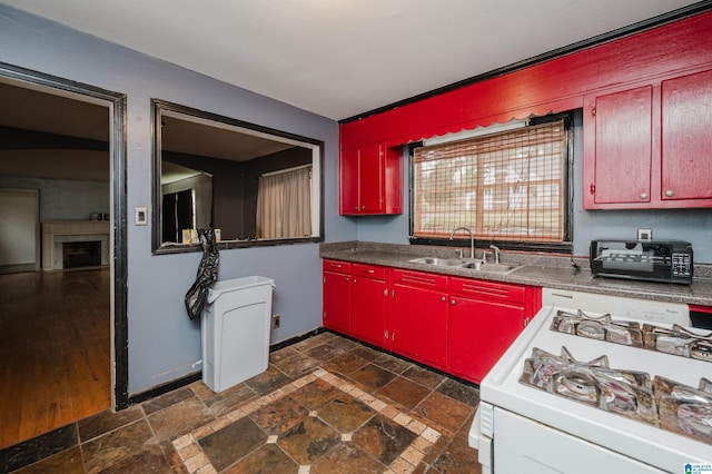 kitchen with a sink, red cabinets, stone tile flooring, and white gas range oven