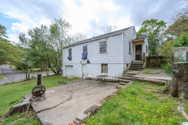 rear view of property featuring a fire pit, an attached garage, fence, and a yard
