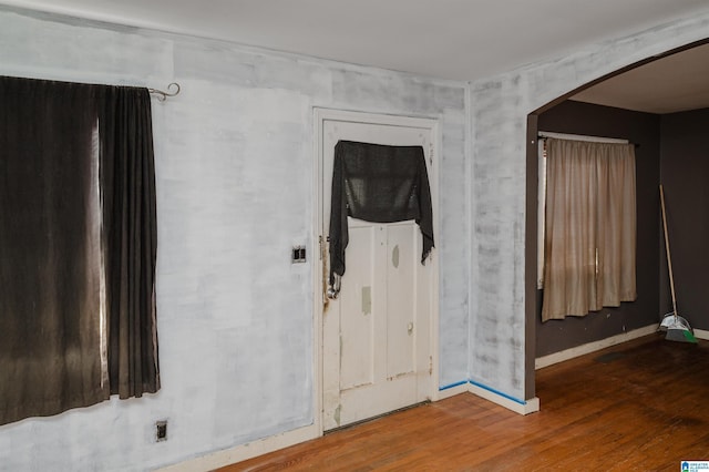 spare room with arched walkways, baseboards, and wood finished floors