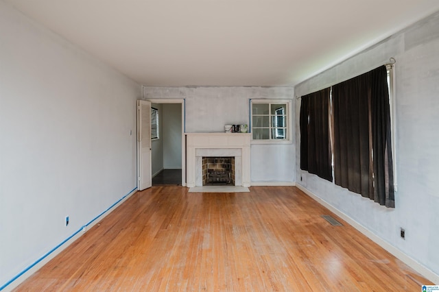 unfurnished living room featuring light wood-style floors, a fireplace with flush hearth, and visible vents