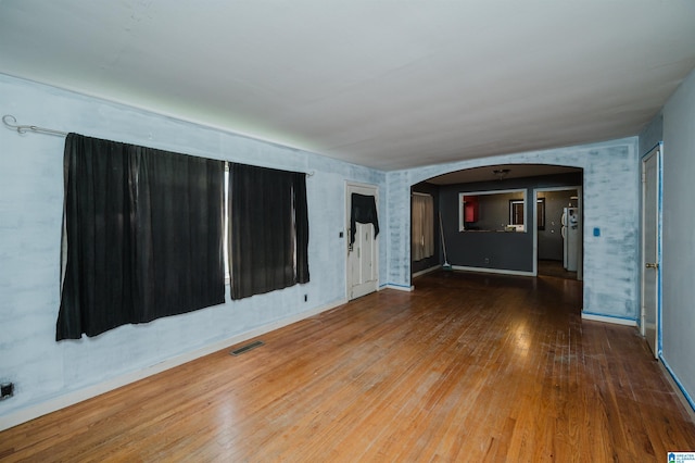 empty room with arched walkways, visible vents, and hardwood / wood-style floors