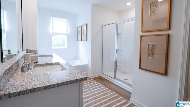 full bath featuring a sink, a shower stall, double vanity, wood finished floors, and a garden tub