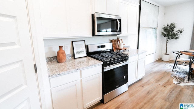kitchen with light wood-style floors, white cabinets, appliances with stainless steel finishes, light stone counters, and baseboards