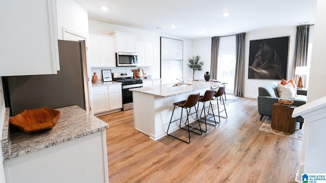 kitchen with white cabinets, appliances with stainless steel finishes, a breakfast bar, a kitchen island with sink, and light wood finished floors