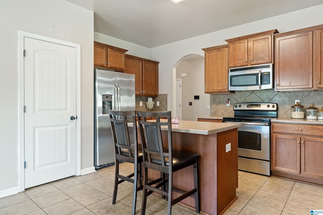 kitchen featuring brown cabinets, appliances with stainless steel finishes, arched walkways, and a kitchen island