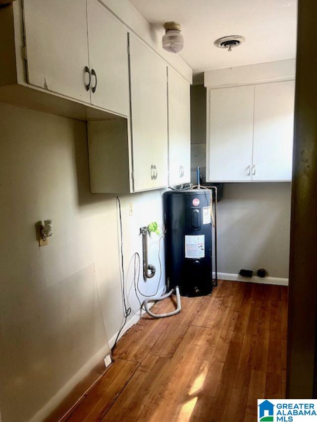 clothes washing area featuring baseboards, water heater, wood finished floors, and visible vents