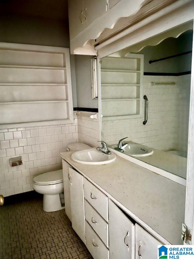 full bathroom with tile walls, wainscoting, tile patterned floors, vanity, and toilet
