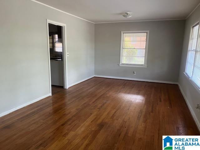 unfurnished room featuring crown molding, dark wood-style flooring, baseboards, and plenty of natural light