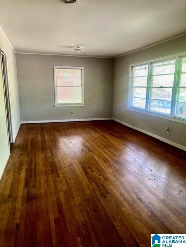 spare room featuring baseboards, wood-type flooring, crown molding, and a wealth of natural light