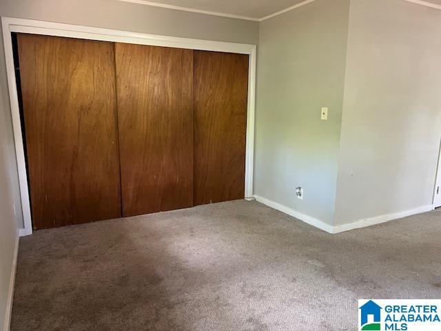 unfurnished bedroom featuring crown molding, baseboards, carpet, and a closet