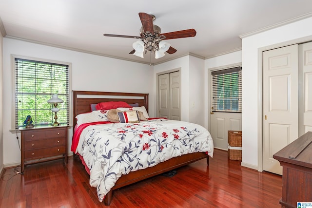 bedroom featuring baseboards, two closets, crown molding, ceiling fan, and wood finished floors