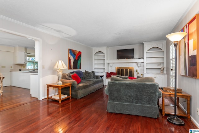 living room with baseboards, built in features, crown molding, a brick fireplace, and wood finished floors