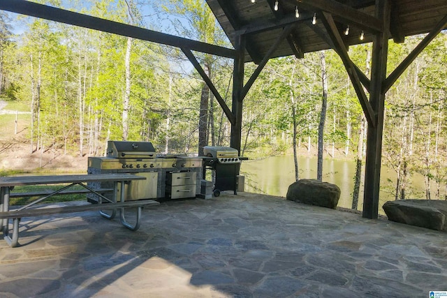 view of patio with a water view, a grill, and a wooded view