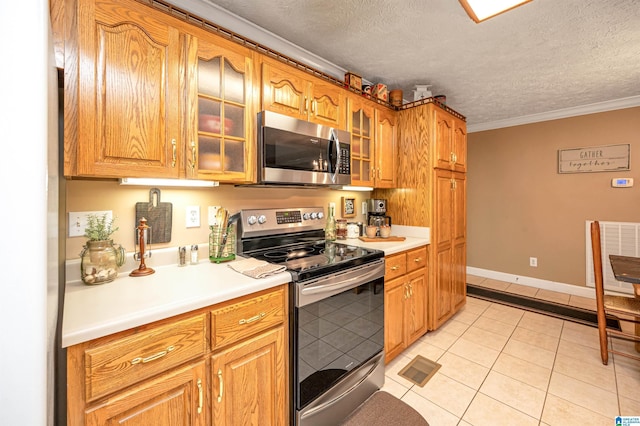 kitchen with light tile patterned floors, glass insert cabinets, light countertops, a textured ceiling, and appliances with stainless steel finishes