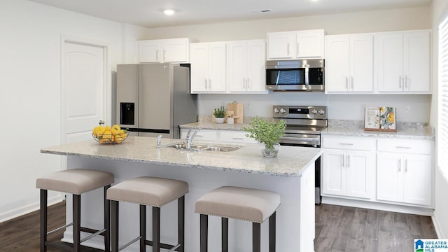 kitchen featuring white cabinetry, a breakfast bar, a kitchen island with sink, a sink, and stainless steel appliances