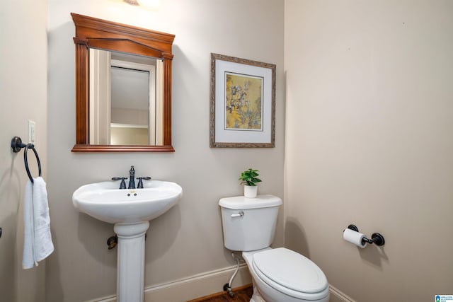 half bath featuring toilet, a sink, and baseboards