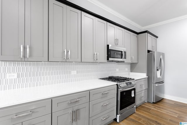 kitchen with gray cabinets, crown molding, appliances with stainless steel finishes, and wood finished floors