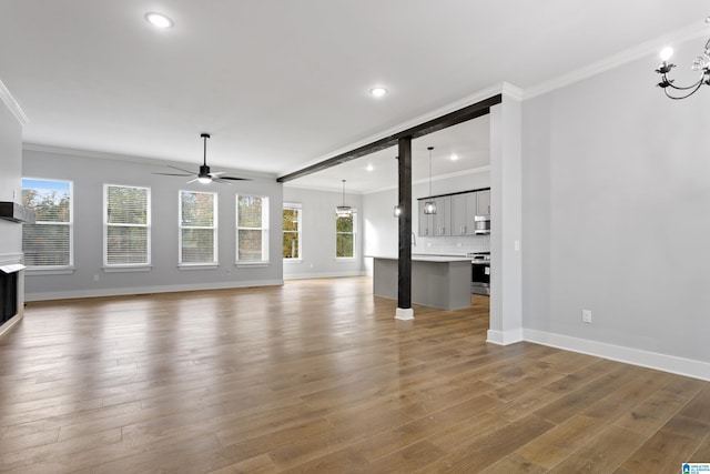 unfurnished living room with crown molding, wood finished floors, ceiling fan with notable chandelier, and a wealth of natural light
