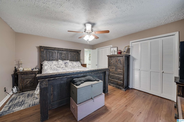 bedroom featuring ceiling fan, a textured ceiling, multiple closets, and wood finished floors