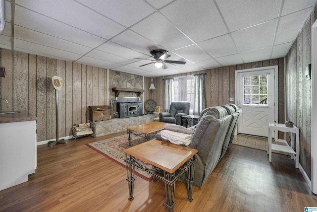 living area featuring wooden walls, ceiling fan, a drop ceiling, and wood finished floors