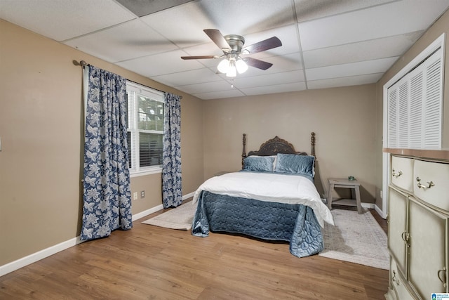 bedroom featuring a ceiling fan, a drop ceiling, visible vents, wood finished floors, and baseboards