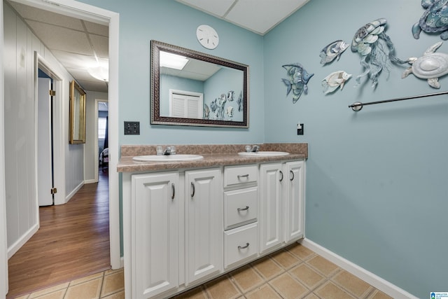 bathroom with a sink, baseboards, double vanity, and a paneled ceiling