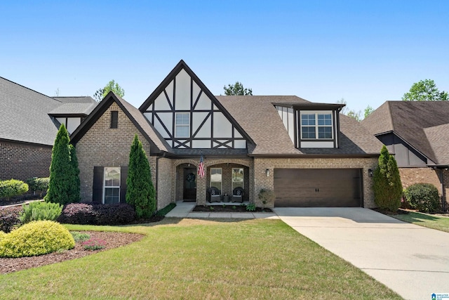 english style home featuring a shingled roof, concrete driveway, a front yard, and brick siding
