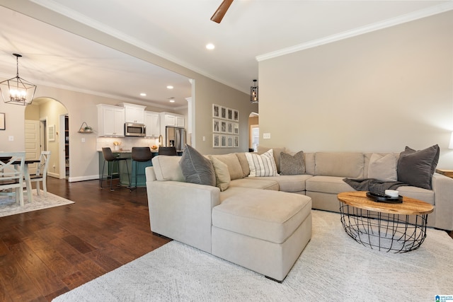 living area with ornamental molding, recessed lighting, dark wood finished floors, arched walkways, and ceiling fan with notable chandelier