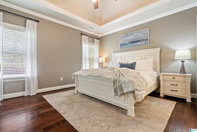 bedroom featuring baseboards, ornamental molding, dark wood-type flooring, a tray ceiling, and ceiling fan
