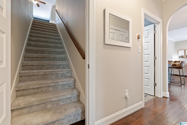 stairs featuring baseboards, arched walkways, ceiling fan, and wood finished floors