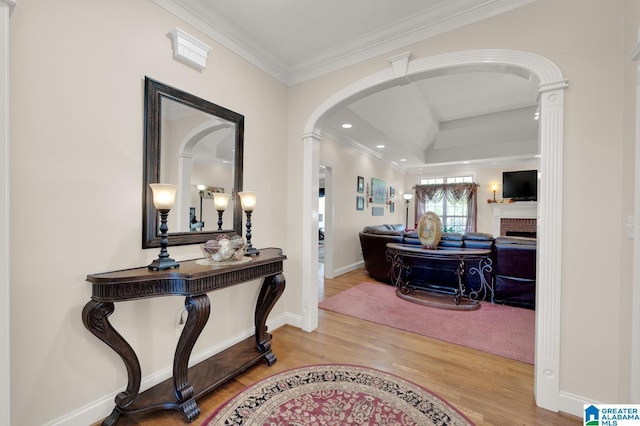 entryway featuring baseboards, arched walkways, a brick fireplace, ornamental molding, and wood finished floors