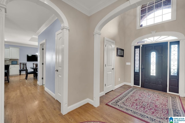 entrance foyer featuring decorative columns, arched walkways, light wood finished floors, and crown molding