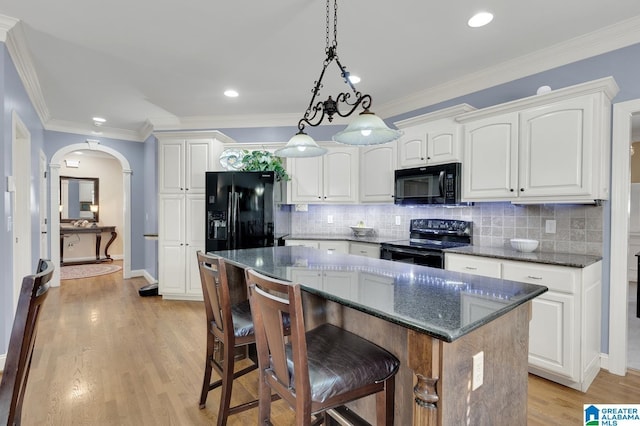 kitchen featuring arched walkways, light wood-style floors, black appliances, backsplash, and a kitchen island