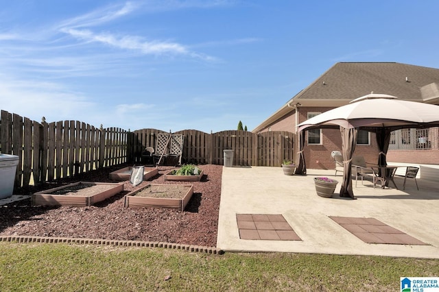 view of yard with a patio area, a fenced backyard, a gazebo, a gate, and a vegetable garden