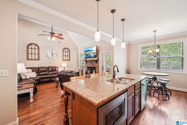 kitchen featuring wood finished floors, a stone fireplace, hanging light fixtures, a sink, and stainless steel appliances